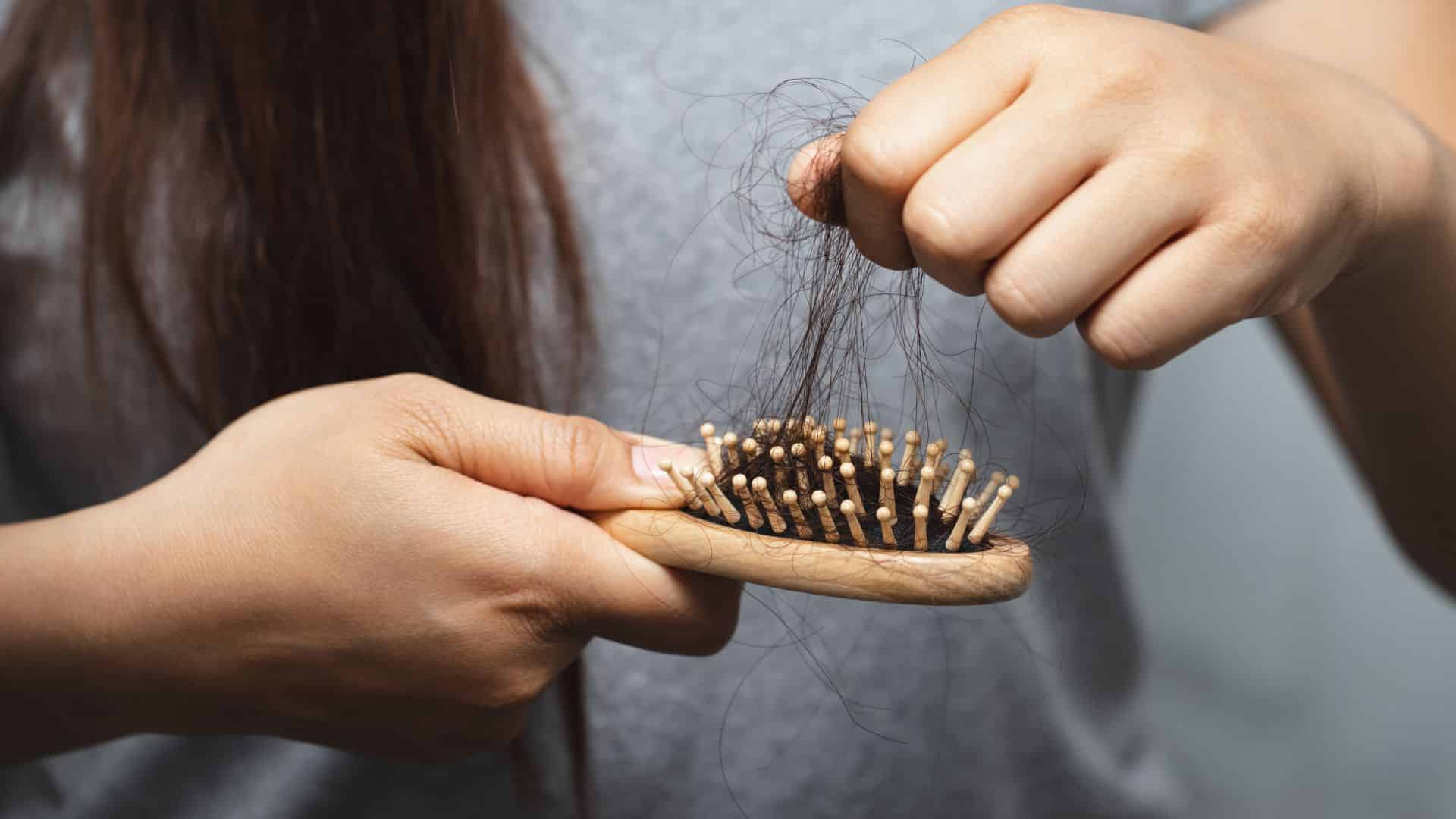 a woman is holding a wooden brush with her hair on it