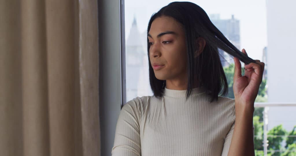 mixed-race-gender-fluid-person-looking-through-window-at-home-SBI-349549684